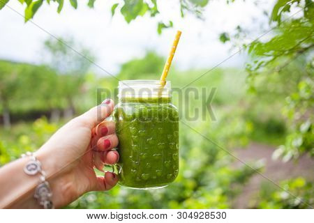 woman's hand holding a jar with green cold-pressed juice, nature background. Healthy eating, detoxing, juicing, body cleancing concept 