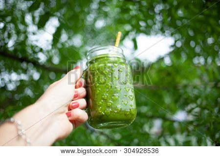 woman's hand holding a jar with green cold-pressed juice, nature background. Healthy eating, detoxing, juicing, body cleancing concept 
