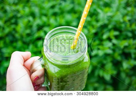 woman's hand holding a jar with green cold-pressed juice, nature background. Healthy eating, detoxing, juicing, body cleancing concept 
