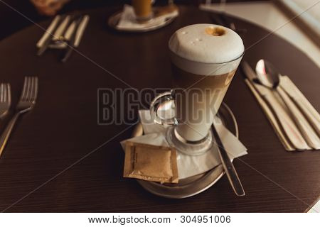 Cup Of Caffe Latte In Coffeehouse On Brown Table With Set Of Cutlery