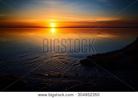 The Creek Flows Into The Lake On A Background Of Windy Sunset