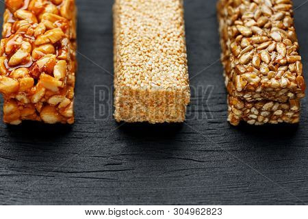 Cereal Granola Bar With Peanuts, Sesame And Sunflower Seeds On A Cutting Board On A Dark Stone Table