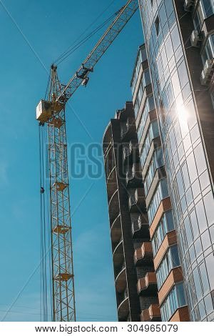 Building Under Construction And Construction Crane Against Blue Sky And Bright Sun On Summer Day. Bo