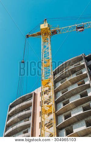 Building Under Construction And Construction Crane Against Blue Sky And Bright Sun On Summer Day. Bo