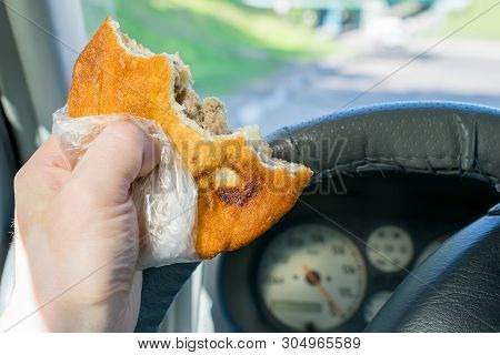 Pie, Belyash With Meat In The Hand Of The Driver In The Car On The Background Of The Steering Wheel 