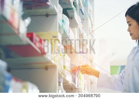 Pharmacist Holds A Packet Of Pills In Her Hands. Then She Shows A Thumbs Up. A Woman Is Standing In 
