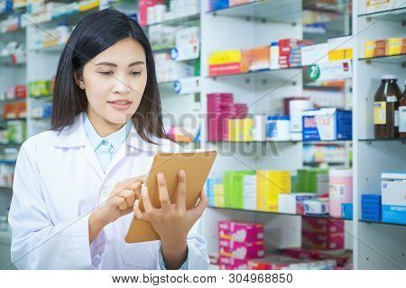 Pharmacist Working With A Tablet Computer In The Pharmacy Holding It In Her Hand While Reading Infor