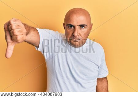 Mature middle east man wearing casual white tshirt looking unhappy and angry showing rejection and negative with thumbs down gesture. bad expression. 
