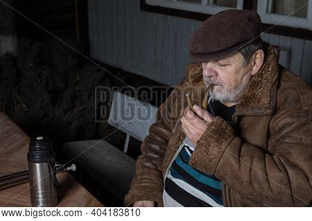 Nice Portrait Of Bearded Caucasian Senior Man Sitting Next To His House With With Tobacco Pipe At Co