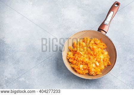 Fry Grated Carrots And Chopped Onions With Oil In A Frying Pan. Gray Concrete Background. Copy Space