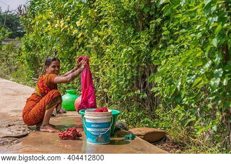Lakundi, Karnataka, India - November 6, 2013: Squatting Young Woman In Orange Sari Doing Laundry Out