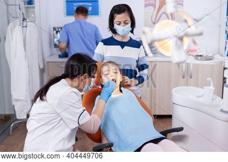 Stomatologist Using Curved Mirror In The Course Of Cavitiy Examination Of Little Girl Wearing Bib. D