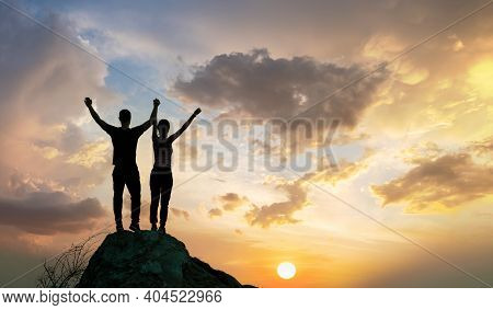 Man And Woman Hikers Standing On A Big Stone At Sunset In Mountains. Couple Raising Up Hands On High