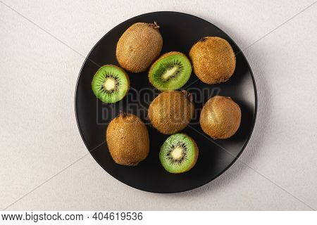 Kiwi Fruits Half Sliced In Black Plate On Vibrant Plain White Background, Copy Space, Top View