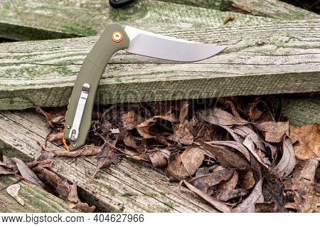 Green Knife Handle On A Green Tree. Knife With A Clip For Carrying. Angle View.