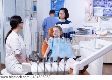 Parent With Little Girl Listening Pediatric Dentist Talking About Mouth Hygine In Dental Office. Chi