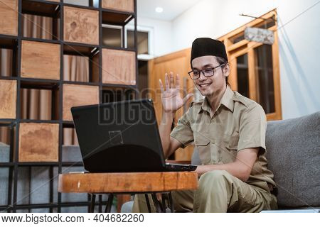 Male Teacher In Civil Servant Uniform And Wearing A Cap Waving In Front Of A Laptop Computer
