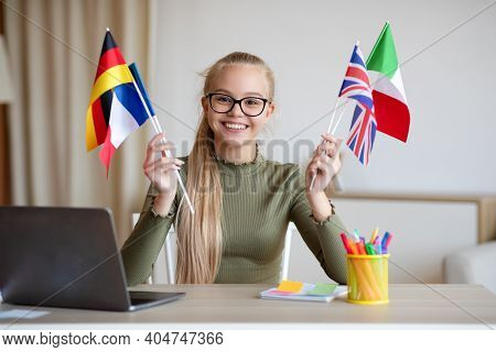 Cheerful Blonde Teen Girl With Glasses Sitting At Workdesk With International Flags, Home Interior, 