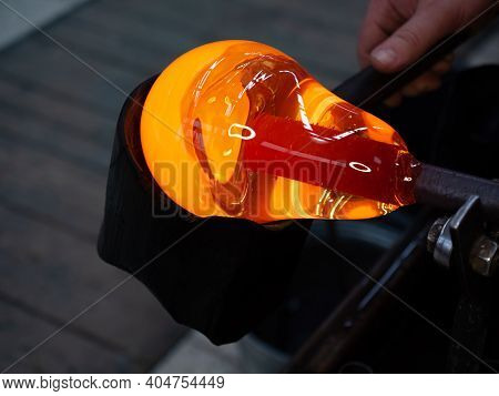 Glassblower Is Using Wet Wooden Form For Shaping The Red Melted Glass On The End Of Glassblowing Pip