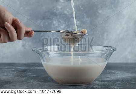 Female Hand Adding Milk Into Strainer Spoon Full Of Cereal Balls