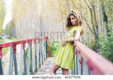 schÃ¶nes blondes MÃ¤dchen, gekleidet mit einem Beige Kleid, in einer lÃ¤ndlichen BrÃ¼cke stehend