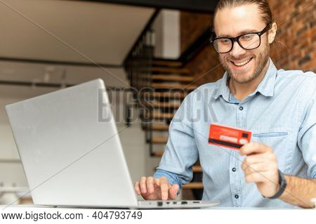 A Guy Is Makes An Order Online, E-shop, Smiles In Anticipation Of The Purchase, A Man Holding Credit