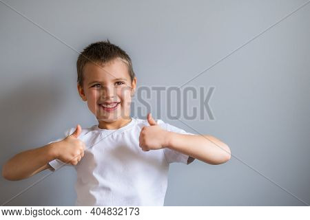 Boy Without Milk Upper Tooth In White T-shirt Showing Thumb Up On The Gray Background.