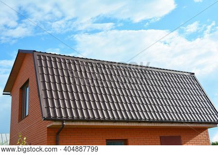 A Close-up Of A Mansard Metal Roof With An Attic Window And Roof Gutters Of A Brick House Constructi