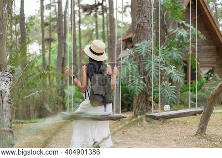 A Female Asian Tourist In White Dress Sits On A Swing, And Enjoys A Vacation In Pine Forest At Doi B