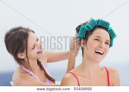 Girl fixing her friends hair rollers at home in bedroom at sleepover