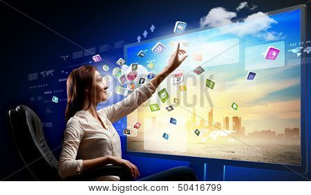 Young woman in armchair pushing icon on media screen
