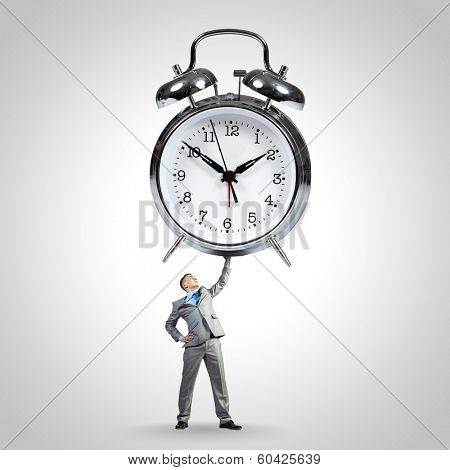 Young strong businessman lifting huge alarm clock above head