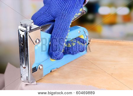 Fastening fabric and wooden box using construction stapler on bright background