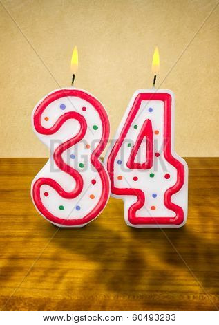 Burning birthday candles number 34 on a wooden background