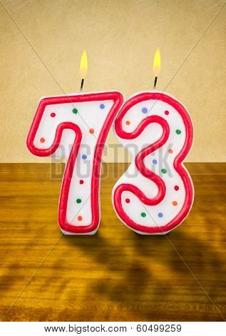 Burning birthday candles number 73 on a wooden background