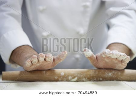 Closeup midsection of a chef rolling dough with rollingpin