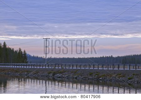 Daybreak up North over a lake, road, forest and hills.