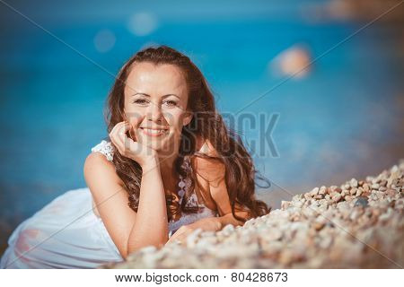 A woman in a light summer dress relaxing on the beach.