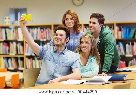 people, technology, friendship, education and school concept - group of happy students with smartphone taking selfie at library