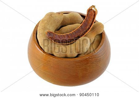 A wooden bowl full of big Tamarind pods (Tamarindus indica) isolated on white