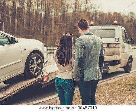 Couple near tow-truck picking up broken car 