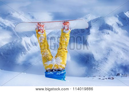 Legs of a snowboarder in yellow trousers stuck in deep snow upside down
