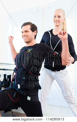 Female personal trainer giving man ems electro muscular stimulation exercise 