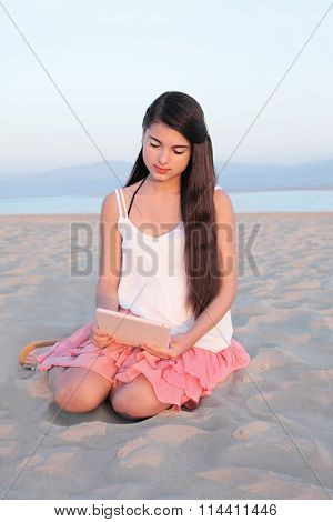 Beautiful young caucasian teenage girl with long dark hair on a tablet computer on a beach in summer.