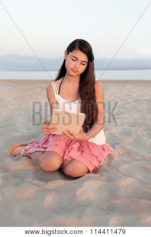 Young teenage girl relaxing on a beach with a tablet computer device.