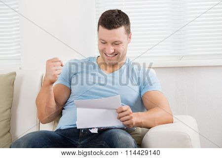 Man Clenching Fist While Reading Letter On Sofa
