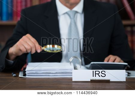 Auditor Examining Documents With Magnifying Glass At Table