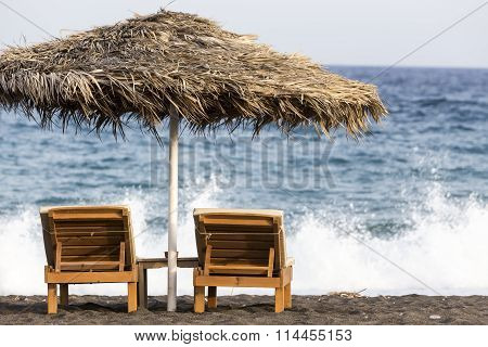 View Of Perissa Beach On The Greek Island Of Santorini With Sunbeds And Umbrellas. Beach Is Covered