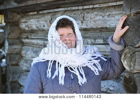 The Russian woman in a shawl warms hands near an izba
