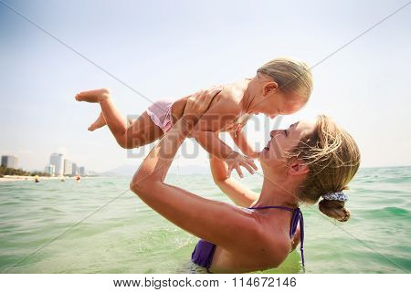 Closeup Side-view Mother Holds Small Daughter Both Smile In Sea
